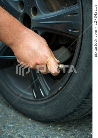 Man's hand inflating tire and checking air pressure with gauge pressure in service station  127842118