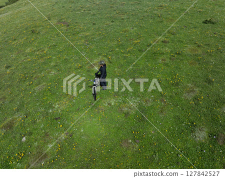 Aerial view of woman riding mountain bike on flowering grassland mountain trail 127842527