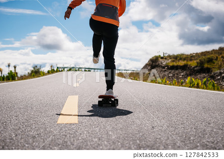 Skateboarder skateboarding on the mountain road Skateboarder skateboarding on the mountain road 127842533