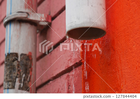 Rainwater Drainage System Flowing Gracefully from PVC Pipe on a Colorful Wall Rainwater Drainage System Flowing Gracefully from PVC Pipe on a Colorful Wall 127844404