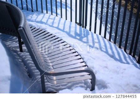 Snow-covered riverside bench and winter river surface Snow-covered riverside bench and winter river surface 127844455
