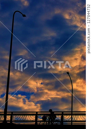 A bicycle crossing an overpass while looking up at the sunset 127844732