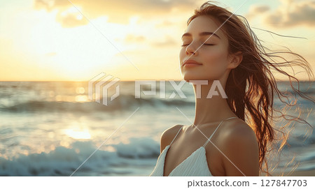 Beautiful woman closing her eyes and feeling the breeze on the beach illuminated by the setting sun Beautiful woman closing her eyes and feeling the breeze on the beach illuminated by the setting sun 127847703