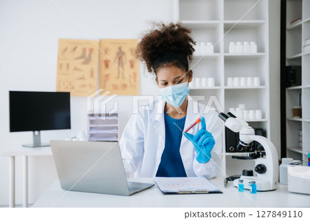 Young scientists conducting research investigations in a medical laboratory, a researcher in the foreground is using a microscope in laboratory for medicine. 127849110