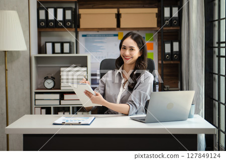 Confident beautiful Asian businesswoman typing laptop computer and digital tablet while holding tablete at office Confident beautiful Asian businesswoman typing laptop computer and digital tablet while holding tablete at office 127849124