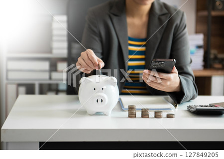 Business woman hand putting money coin into piggy bank with step of growing stack coins for saving money with virtual icon 127849205