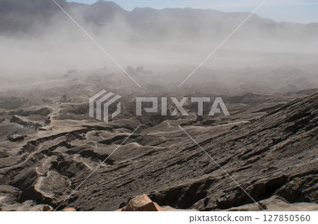 The rough surface, with layers of rocks piled on top of each other far into the distance. Covered by a sandstorm around the mountain Bromo, Indonesia 127850560