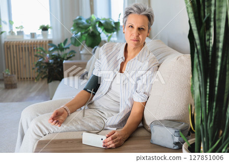 Senior woman checking blood pressure at home, looking concerned about health condition 127851006