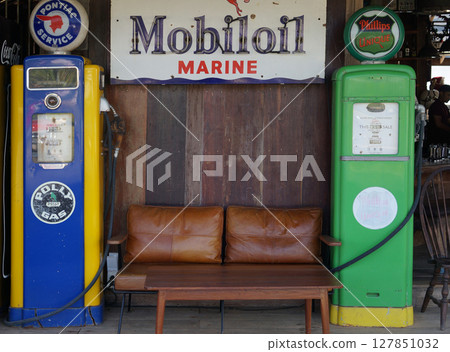 A nostalgic scene featuring two classic gas pumps, an oil sign, and a wooden bench, evokes the charm of a bygone era. 127851032