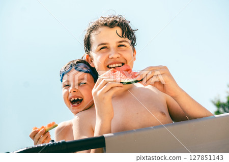 Two happy boys eating juicy watermelon and laughing together under bright summer sunshine Two happy boys eating juicy watermelon and laughing together under bright summer sunshine 127851143