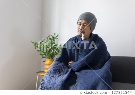 Asian man sick or ill and coughing by covering their mouth with napkin paper while sitting on the sofa at home. 127851544