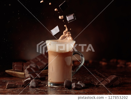 Pieces of bitter chocolate fall in glass mug with cocoa drink. 127853202