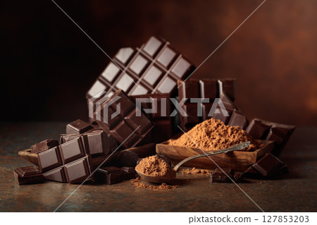 Scraps of dark chocolate next to a wooden bowl of cocoa powder. 127853203