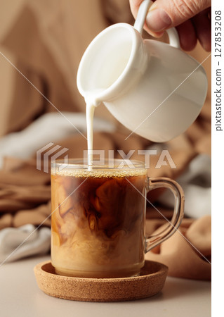 Pouring cream in black coffee. 127853208
