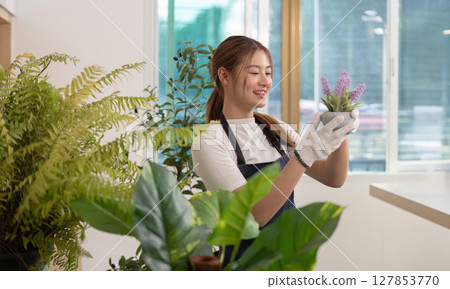 Indoor Gardening Joy. Young woman caring for potted plants with a smile. 127853770