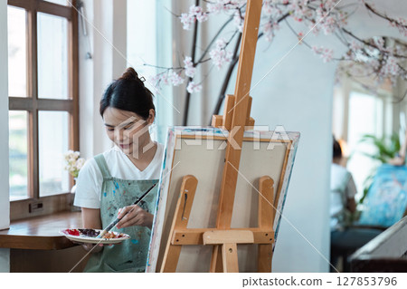 Young Woman Engaged in Painting at Home Studio with Blossoming Cherry Tree in Background, Showcasing Creative Hobby and Artistic Passion in a Bright and Serene Environment 127853796