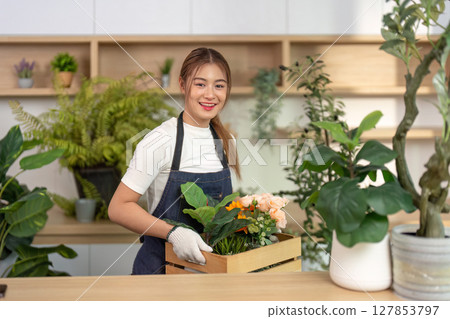 Floral Arrangement and Plant Care. Young woman carrying a box of flowers in a bright indoor space. 127853797