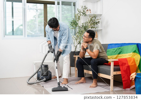 Teamwork in Cleaning. Two friends organizing their living area with a rainbow flag in the background. Teamwork in Cleaning. Two friends organizing their living area with a rainbow flag in the background. 127853834