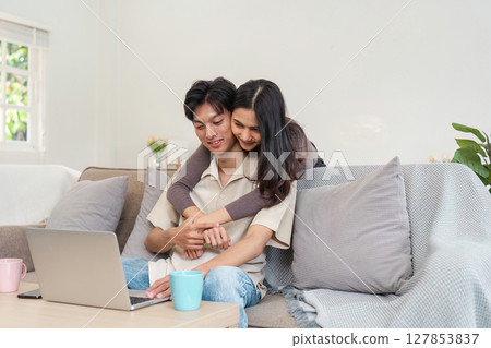 Young Couple Enjoying Quality Time Together at Home, Relaxing on the Couch with a Laptop, Smiling and Embracing in a Cozy Living Room Setting, Perfect for Lifestyle and Home Comfort Themes Young Couple Enjoying Quality Time Together at Home, Relaxing on the Couch with a Laptop, Smiling and Embracing in a Cozy Living Room Setting, Perfect for Lifestyle and Home Comfort Themes 127853837