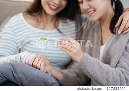 Two happy gay lesbian lgbt women couple sitting on sofa celebrating positive pregnancy test. lgbtq concept Two happy gay lesbian lgbt women couple sitting on sofa celebrating positive pregnancy test. lgbtq concept 127853911