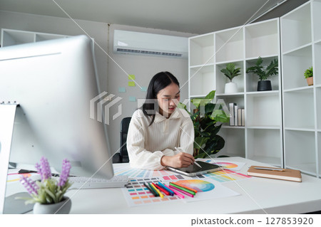 designer graphic at work drawing sketches a new project on graphic tablet and color palette sitting at desk with computer at studio or office 127853920