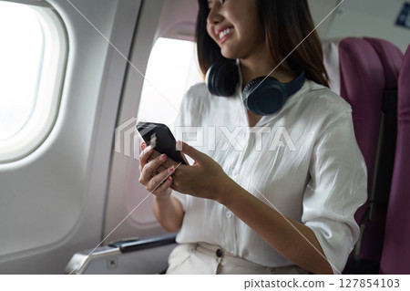 Beautiful Asian in aeroplane. working, travel, business concept Traveler on Plane Using Smartphone with Headphones, Smiling and Happy 127854103