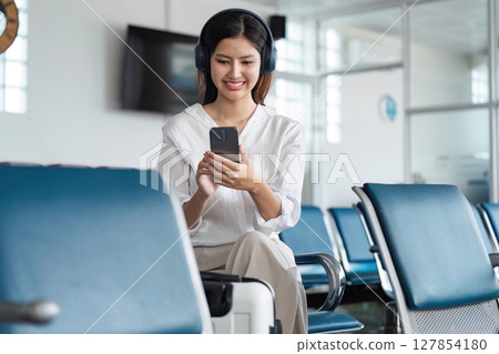 Woman listening to music on headphones in airport lounge, use smartphone and earphones while waiting for her flight Woman listening to music on headphones in airport lounge, use smartphone and earphones while waiting for her flight 127854180