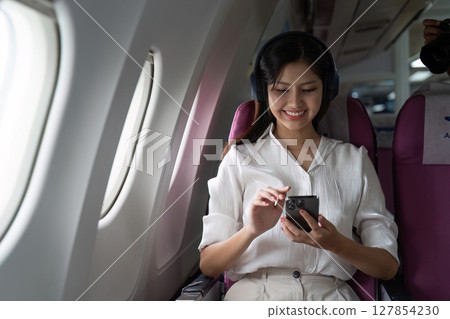 Asian business woman on aeroplane using smartphone Asian business woman on aeroplane using smartphone 127854230