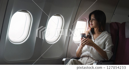 Asian business woman on aeroplane using smartphone 127854233