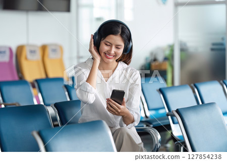Woman listening to music on headphones in airport lounge, use smartphone and earphones while waiting for her flight 127854238