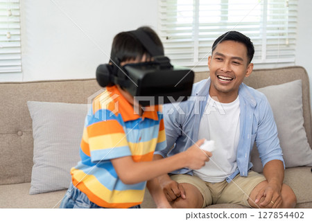 Exciting VR Gameplay. Child immersed in virtual reality gaming with father watching. 127854402