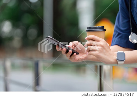 Doctor enjoying coffee while checking smartphone outdoors Doctor enjoying coffee while checking smartphone outdoors 127854517