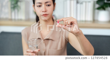 Medication Decision. Woman holding a capsule and glass of water, contemplating. 127854528