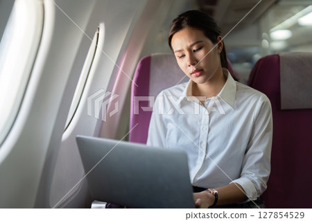 Remote Work on Airplane. Businesswoman using laptop while traveling. 127854529