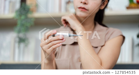 Health Monitoring. Woman checking her temperature with a digital thermometer at home. 127854535