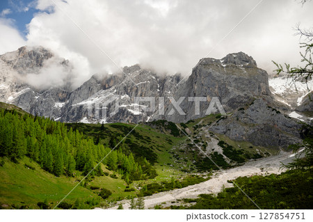 Dramatic Dachstein mountain peaks with lush green valley and clouds in Austria 127854751