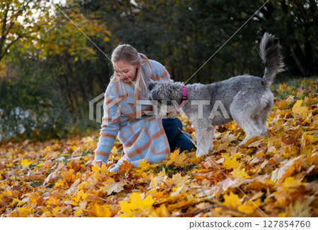 Smiling woman in coat with her mixed-breed dog enjoying autumn leaves in a park Smiling woman in coat with her mixed-breed dog enjoying autumn leaves in a park 127854760