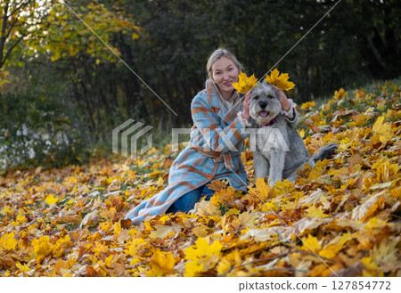 Smiling woman in coat with her mixed-breed dog enjoying autumn leaves in a park 127854772
