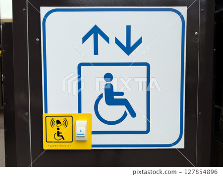Sign indicating an accessibility elevator for people with disabilities, featuring up and down arrows, wheelchair symbol and yellow call button with braille and alert icon for assistance 127854896