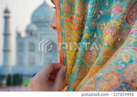 A woman in a blue and orange dress is standing in front of a large building 127854958
