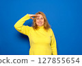A smiling and proud Caucasian woman in her 40s saluting the camera in an act of honor and patriotism, showing respect. Isolated on a blue background 127855654