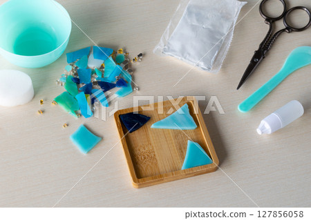 Colorful glass-like fragments prepared for DIY mosaic coaster in silicone mold with gypsum powder and craft tools on table before pouring process begins, step 1 Colorful glass-like fragments prepared for DIY mosaic coaster in silicone mold with gypsum powder and craft tools on table before pouring process begins, step 1 127856058