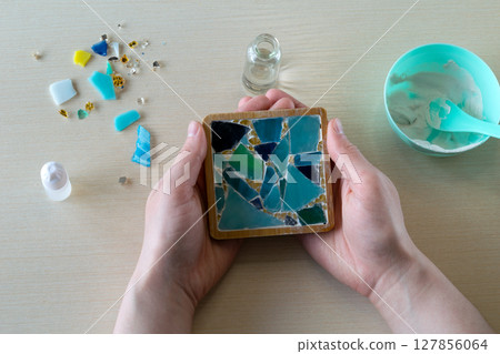 Completed handmade mosaic coaster in mold with dried white gypsum and embedded decorative glass-like fragments viewed from top, step 6 127856064