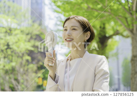 Young businesswoman in an office district holding a handheld fan 127856125