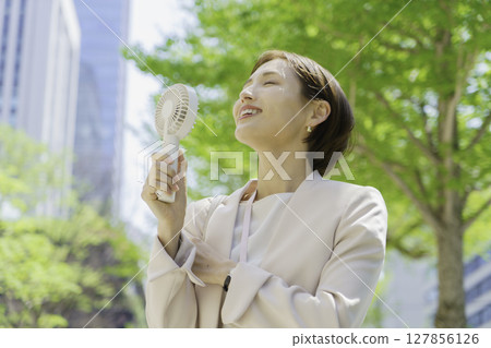 Young businesswoman in an office district holding a handheld fan 127856126