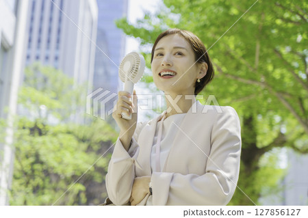 Young businesswoman in an office district holding a handheld fan Young businesswoman in an office district holding a handheld fan 127856127