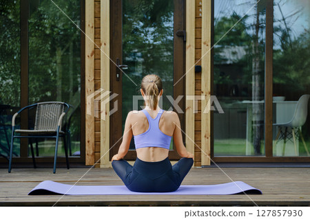 Back view of a woman sits on a yoga mat placed on a wooden terrace of tiny house 127857930