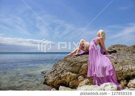 Beach Rocks Woman: Blonde woman poses in a dress on rocks at a sunny beach for beauty and relaxation. 127858328