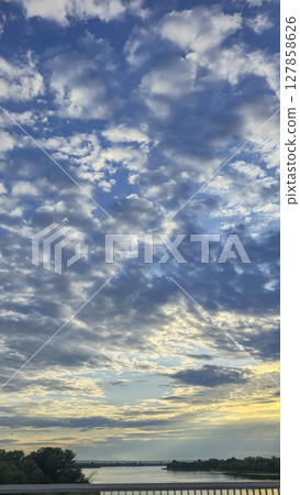 Dark blue sky with clouds over trees and water surface. Evening sunset. 127858626