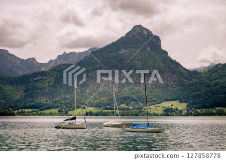 Sailboats anchored on alpine lake with dramatic green mountains and cloudy sky in Austria 127858778
